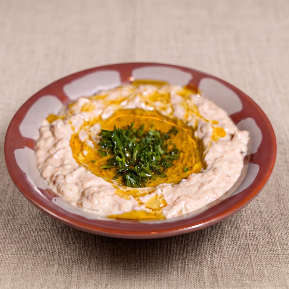 Creamy hummus topped with olive oil and fresh parsley, surrounded by a white garlic sauce on a decorative plate.